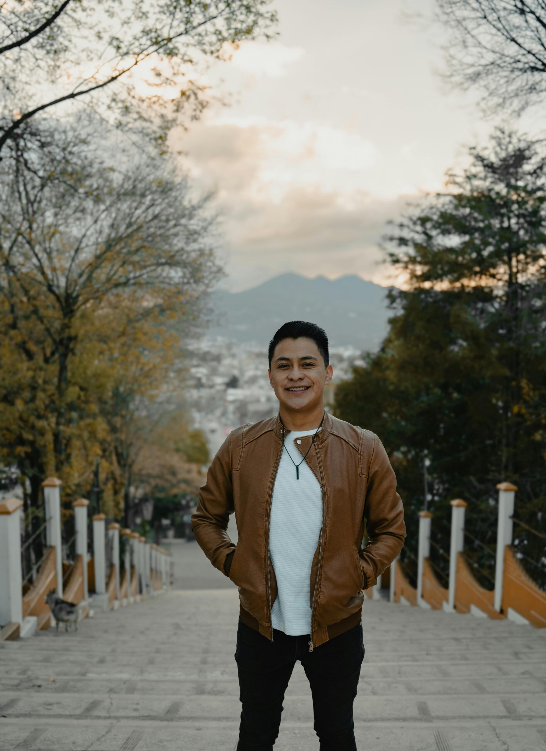 Man smiling on stairs in San Cristóbal de las Casas, surrounded by trees and mountains.